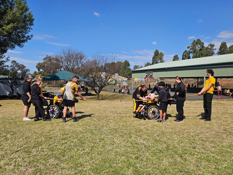 group of students doing tug of war with other students in backgroud playing games on multi purpose courts